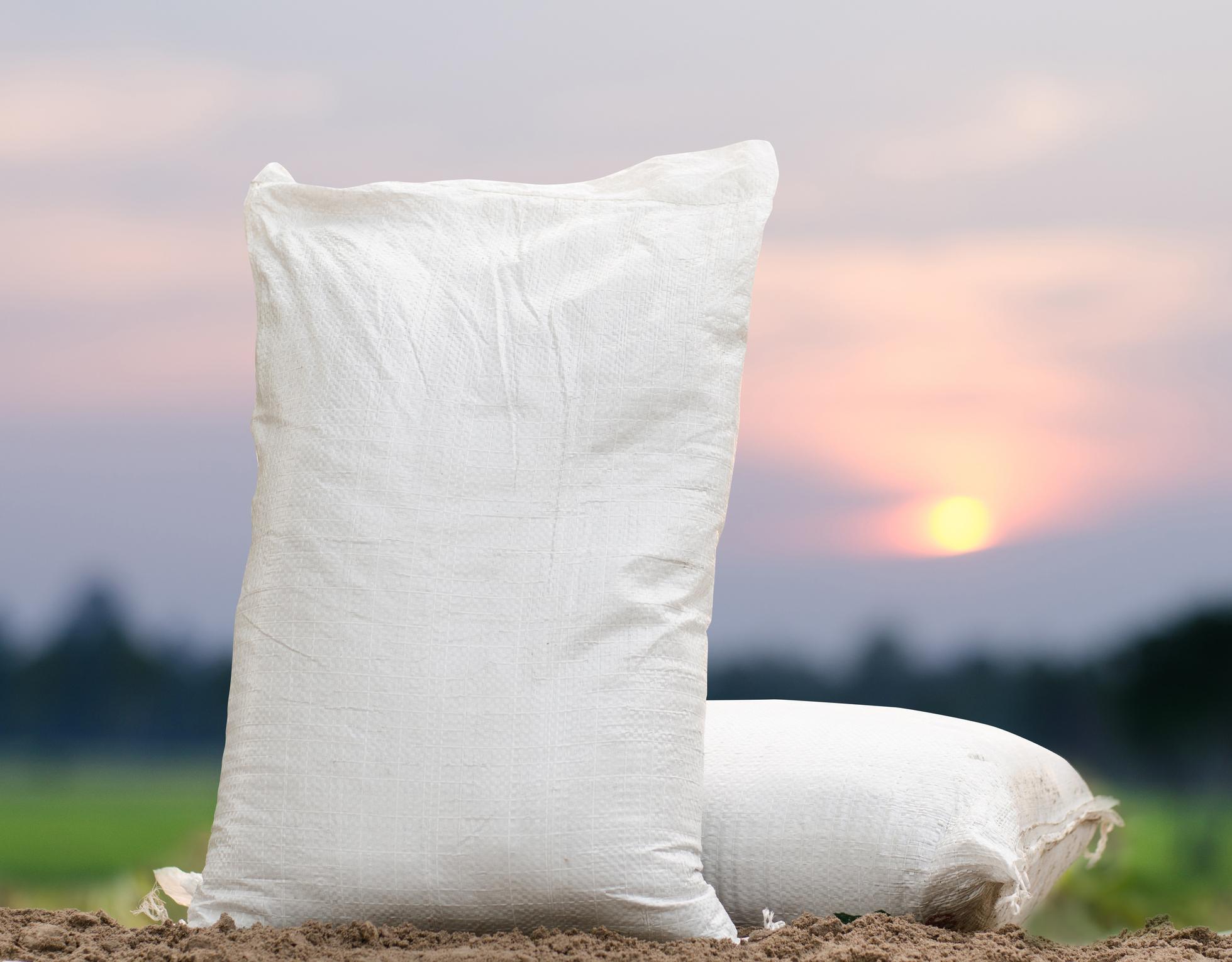 White woven sacks on farmland at sunset, suitable for fertiliser and chemical packaging.